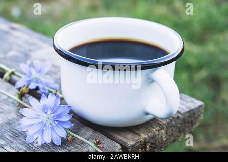 Tasse mit Zichoriengetränk und blauen Zichorienblumen auf einem Holztisch. Zichorienpulver. Gesundes Esskonzept. Kaffee-Ersatz. Stockfoto