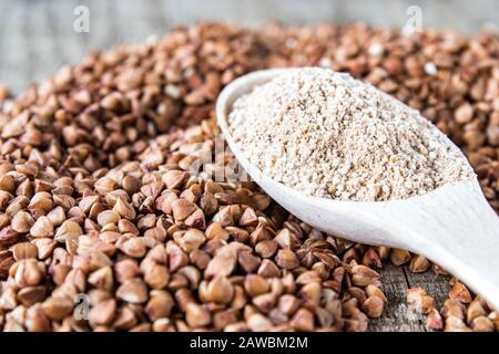 Buchweizenmehl in einem Holzlöffel auf einem Haufen gerösteter Buchweizen. Ein Haufen Buchweizenmehl. Stockfoto