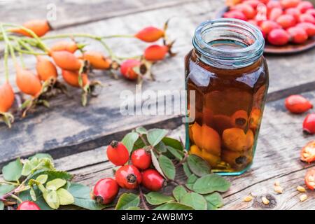 Tinktur oder Getränk mit wilder Rose in einer Glasflasche in der Nähe reifer roter Rosettenbeeren. Phytotherapie. Stockfoto