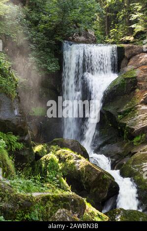 Ein Wasserfall, der über eine Felskante fließt, während die Morgensonne den Dunst erleuchtet. Stockfoto