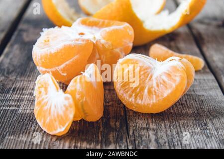 Geschälte Mandarine ohne Schale und Scheiben reifer Mandarine stehen auf dem Tisch. Citruszangen oder Orangen. Nahaufnahme. Stockfoto