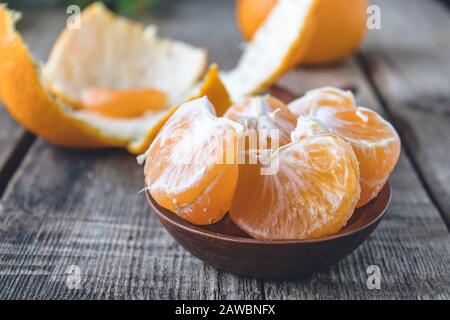 Scheiben von reifen gelben Tangerinen liegen in einer Schüssel nahe der Tangerinschälung auf einem Holztisch. Zitrusfrüchte, Mandarinen oder Orangen. Nahaufnahme. Stockfoto