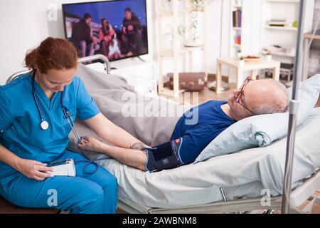 Frauenarzt liest Blutdruck des alten Mannes auf digitalem Gerät im Pflegeheim. Stockfoto