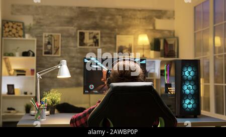 Spielerin feiert Sieg mit erhobenen Händen bei Computerspielen. Mann, der sich auf dem Sofa entspannt und im Hintergrund fernsehen sieht. Stockfoto