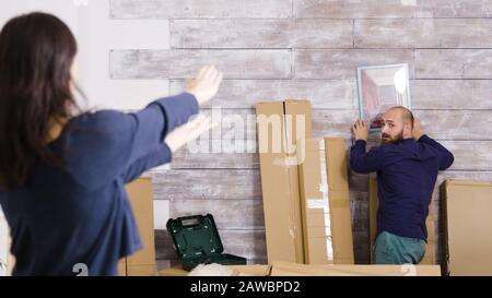 Kaukasische Paare hängen Bild an der Wand der neuen Wohnung. Paare schmücken Wohnung. Stockfoto