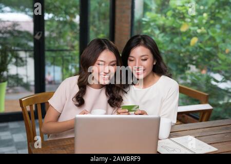 Zwei junge asiatische Frauen, die einen Laptop zum Online-Shopping im Coffeeshop verwenden. Stockfoto