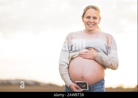 Eine schwangere Frau hält ein Foto von ihrem Baby Ultrasound im Freien. Stockfoto