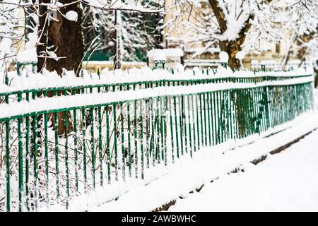 Grüner metallischer Zaun mit Schnee. Metallzaun im Winter mit Schnee bedeckt. Schneebedeckte Umgebung am Morgen Stockfoto