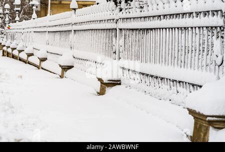 Metallischer Zaun mit Schnee. Metallzaun im Winter mit Schnee bedeckt. Schneebedeckte Umgebung am Morgen Stockfoto