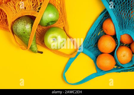 Mandarinen und grüne Äpfel im Saitenbeutel auf gelbem Hintergrund. Kein Abfall, Kunststofffreies Konzept. Gesunde, saubere Ernährung und Entgiftung. Sommerfrüchte. Stockfoto