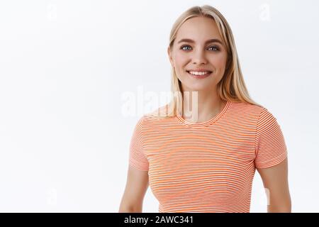 Sorgenfreie, attraktive Frau im gestreiften T-Shirt mit blauen Augen, sieht schön und zart aus, lächelt fürsorglich und freundlich, drückt Liebe und Glück aus Stockfoto