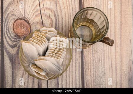 Teebeutel in einer Glasvase und einem leeren facettierten Glas in einem Vintage-Cup-Halter auf Holzhintergrund. Nahaufnahme Stockfoto