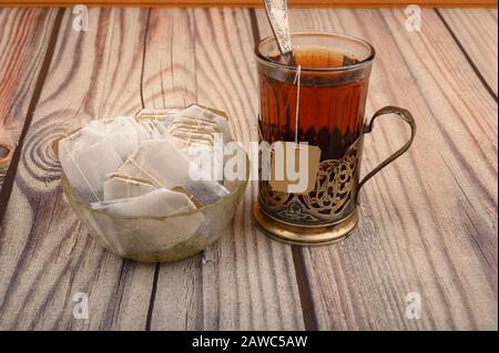 Tee aus facettiertem Glas in einem Vintage-Cup-Halter und Teebeutel in einer Glasvase auf Holzhintergrund. Nahaufnahme Stockfoto