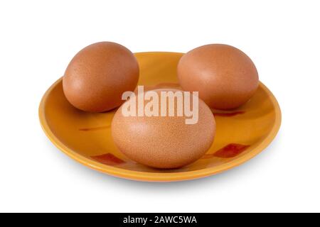 Drei braune Hühnereier liegen auf einem Teller auf weißem Grund. Zutaten zum Backen. Stockfoto