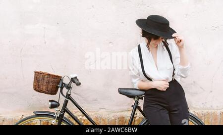 Das Mädchen im Hut, das mit dem Fahrrad gegen die Wand steht. Stockfoto