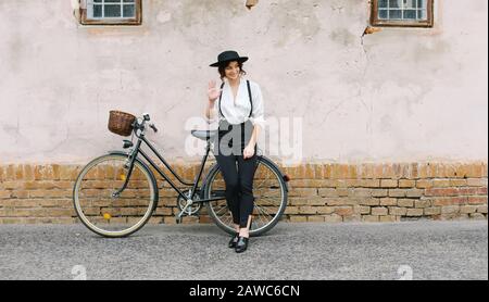 Das Mädchen im Hut, das mit dem Fahrrad gegen die Wand steht. Stockfoto