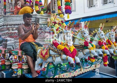 Während des Hindu-Festivals in Thaipusam sitzt ein Teilnehmer auf einem festlichen Wagen mit seinem Handy, Singapur Stockfoto