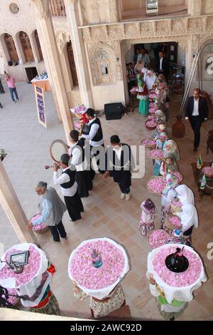 Iranische Männer und Frauen in lokalen Kostümen beim Rosenfest in Kashan, tragen Körbe mit Rosen und Rosenwasser über den Kopf und spielen Musik Stockfoto