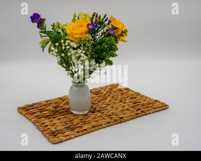 Lila, Gelb und Grün Blumenarrangement in einer weißen Glasvase, die auf einem braunen, weissen Hintergrund sitzt. Stockfoto