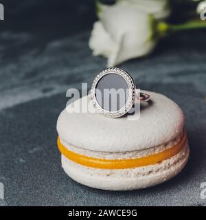 Zarte Ohrringe liegen auf dem rosafarbenen Makronen mit goldenen Ringen auf dem Hintergrund Stockfoto