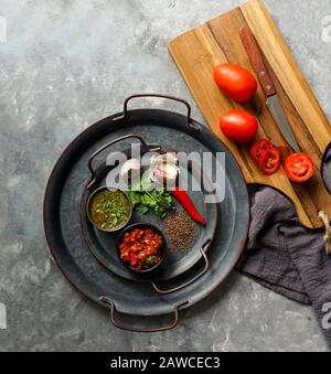 Kolumbianische Küche, aji picante, hogao salsa, auf der Metallschale und Zutaten für Souce, auf der grauen Betonkulisse, Platz für Designtext Stockfoto