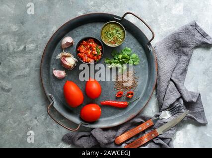 Kolumbianische Küche, aji picante, hogao salsa, auf der Metallschale und Zutaten für Souce, auf der grauen Betonkulisse, Platz für Designtext Stockfoto