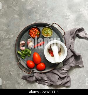 Kolumbianische Küche, aji picante, hogao salsa, auf der Metallschale und Zutaten für Souce, auf der grauen Betonkulisse, Platz für Designtext Stockfoto