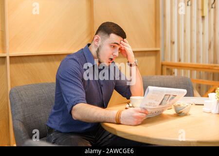 Junger überraschter Mann liest Zeitung Stockfoto