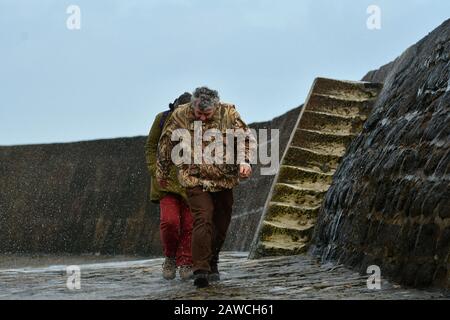 Lyme Regis, Dorset, Großbritannien. Februar 2020. Großbritannien Wetter, Menschen laufen für Deckung entlang der cobb-wellenbrecher, während das Meer über der Spitze weht. Bildnachweis Robert Timoney/Alamy/Live/News Stockfoto