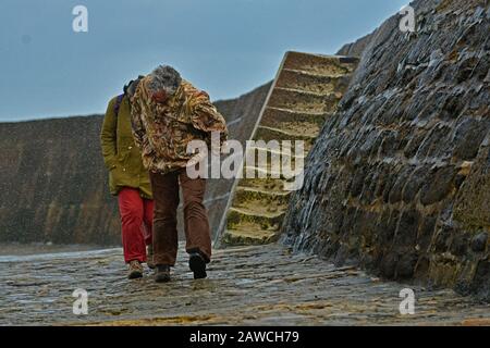 Lyme Regis, Dorset, Großbritannien. Februar 2020. Großbritannien Wetter, Menschen laufen für Deckung entlang der cobb-wellenbrecher, während das Meer über der Spitze weht. Bildnachweis Robert Timoney/Alamy/Live/News Stockfoto