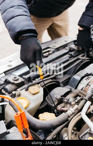 Mann mit schwarzen Handschuhen, der den Ölstand im Auto im Winter im Freien überprüft. Kfz-Mechaniker, der im Kfz-Reparaturdienst arbeitet. Stifthände zur Befestigung eines Autos Stockfoto