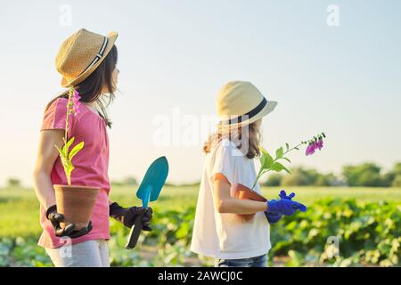 Porträt zweier kleiner Gärtner in Handschuhen mit blühenden Pflanzen in Töpfen und Gartenschaufeln Stockfoto