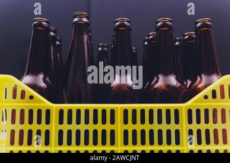 Staubige gelbe Bierkiste aus Vintage-Gelb mit leeren braunen Bierflaschen auf weißem Hintergrund Stockfoto