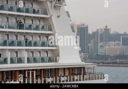 Passagiere stehen auf einem Balkon an Bord des Dream World Cruisers, der in den letzten 3 Tagen in Hongkong am Kai Tak Cruise Terminal in der Kowloon Bay anlegt. Die Behörden halten 3.600 Passagiere und Besatzungsmitglieder unter Quarantäne. Stockfoto