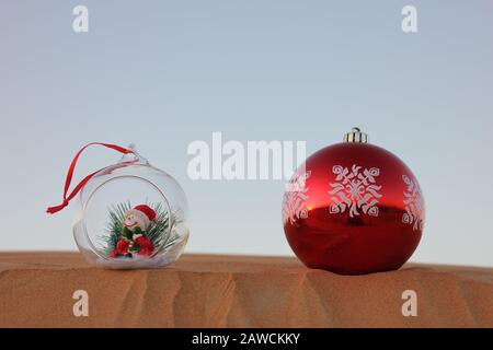 Weihnachtskugeln auf einer Sanddüne in der Wüste in Dubai, Vereinigte Arabische Emirate. Bild für frohe Feiertage/Weihnachtsgrüße Konzept mit Platz für Text kopieren. Stockfoto