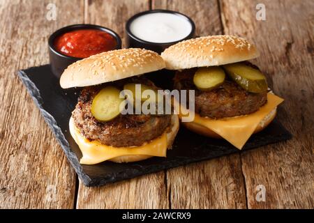 Straßennahrung Oklahoma gebratene Zwiebelburger mit Cheddar-Käse und Pickeln liegen auf einer Schiefertafel auf einem Tisch. Horizontal Stockfoto