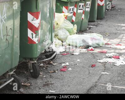 Abgebrochener Müll. Mülleimer stehen in einer Reihe und können auf einer Wohnstraße gesammelt werden. Am Boden Müllsäcke, die Verschmutzung verursachen und d Stockfoto