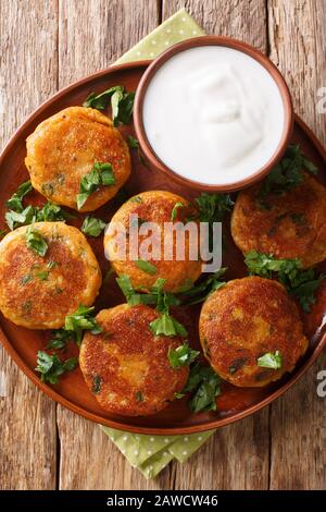 Aloo tikki ist ein beliebter nordindischer Imbiss aus gewürzten, frischen Kartoffelpatten mit Joghurt aus nächster Nähe auf einem Teller auf dem Tisch. Vertikale Draufsicht von oben Stockfoto