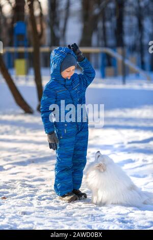 Kleiner Junge trainiert im Winter einen Spitzhund im Park Stockfoto