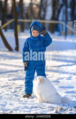 Kleiner Junge trainiert im Winter einen Spitzhund im Park Stockfoto