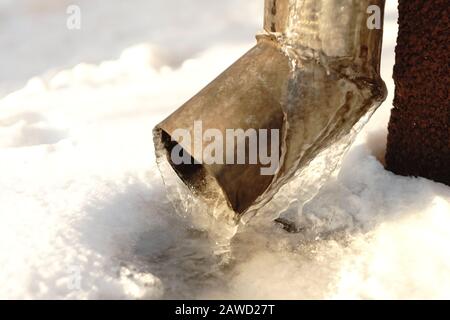 Drainpipe an der Ecke des Hauses mit Eis und Eiszapfen bedeckt Stockfoto