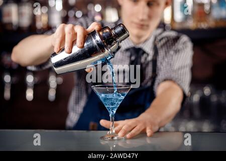 Barman bereitet einen blauen Cocktail aus Martiniglas vor. Spritzer, dunkler Hintergrund. Stockfoto