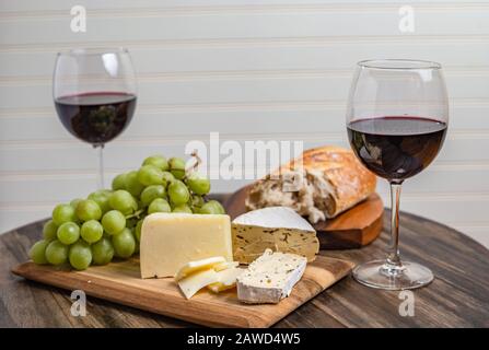 Wein- und Käseplatte serviert mit Trauben auf Holzoberfläche mit weißem Hintergrund Stockfoto