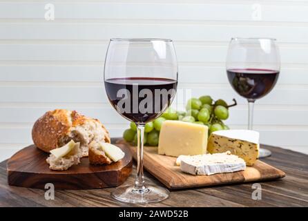 Wein- und Käseplatte serviert mit Trauben auf Holzoberfläche mit weißem Hintergrund Stockfoto