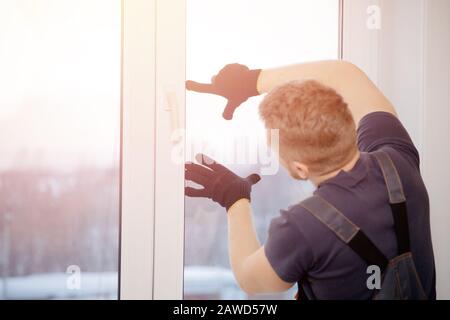 Der männliche Bauherr installiert und überprüft Kunststofffenster im Wohnhaus. Stockfoto