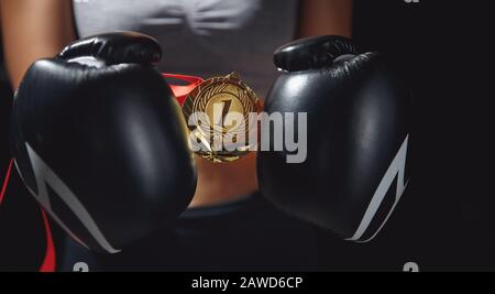 Boxhandschuhe halten die Goldmedaille an erster Stelle in den Händen der weiblichen Gewinnerin. Stockfoto