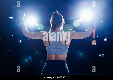 Gewinnerin Junge Boxersportlerin hält Goldmedaille in der Hand auf dunkel verschwommenem Hintergrund, Foto von hinten. Stockfoto