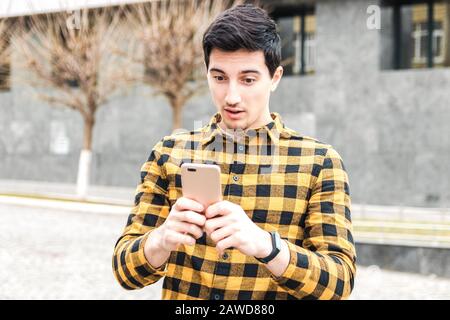 Junger Mann in gelbem Hemd, der im Telefon von einem Post oder einer Nachricht schockiert aussieht. Stockfoto