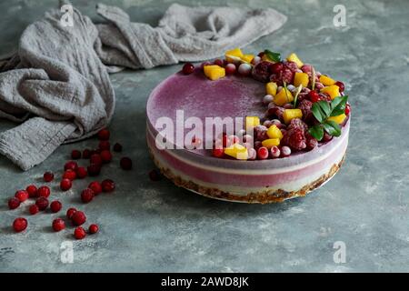 Veganer roher Käsekuchen mit Blaubeere, Kirsche, Matchtee, Orange, Cashew-Creme, Kokosbutter und Kokosmilch sowie Basis aus Mandeln, Datteln und Stockfoto