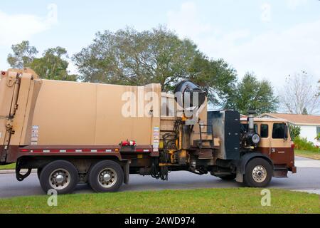 Großer brauner Müllwagen mit hydraulischem Roboterarm, der Müll in einen Kompaktwagen in einem Wohnviertel einlässt. Stockfoto